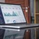 Un ordinateur portable affichant un tableau de bord avec des analyses, des graphiques et des statistiques. L'écran affiche des graphiques linéaires en forme de montagne et des diagrammes à secteurs, indiquant les tendances des données. L'appareil est placé sur une surface réfléchissante dans un environnement de bureau.